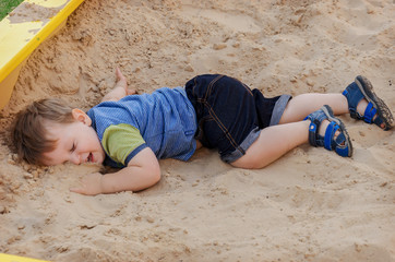 Charming cute boy playing in the sandbox on the playground