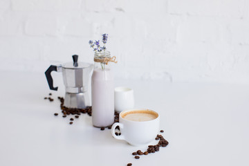 french press, cup of coffee, milk jar and lavender drink with scattered coffee beans on white table