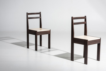 Two classic dark wooden chairs with white top standing in row on white floor in studio