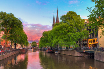 Fototapeta na wymiar Beautiful sunset at the Singel canal in Amsterdam with the Krijtberg church and a tourist boat 