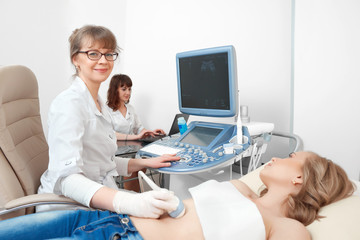 Cheerful mature female doctor smiling to the camera examining her female patient using ultrasound scanning machine people profession occupation gynecology pregnancy analyzing concept.