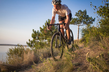Naklejka na ściany i meble Bicycle rider on professional cyclocross bike ride downhill, pine and lake background 