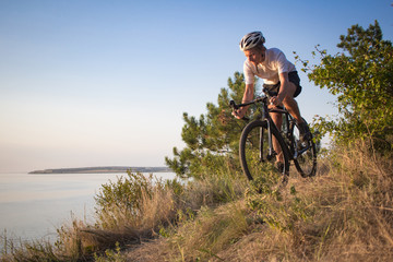 Bicycle rider on professional cyclocross bike ride downhill, pine and lake background 