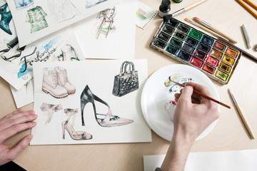 Fashion designer mixes colours of paint in process of drawing fashion sketches of footwear and...