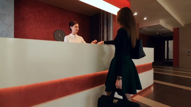 Girl is giving passport to receptionist and taking the key card. Hotel lobby. 4K.