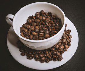 Roasted coffee beans in white cup on dark background. Selective focus.