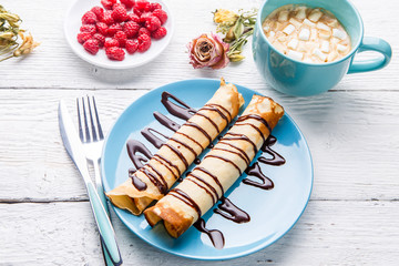 Homemade pancakes or russian blini with chocolate sauce on plate on white wooden background.