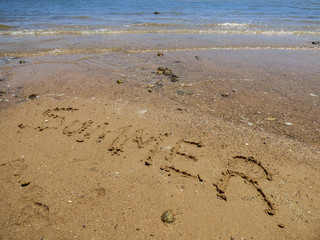 The word Summer written on the sand at the beach, ocean in the background