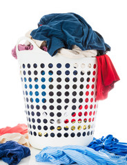 Colorful clothes in white laundry plastic clothes basket beside messy stack clothes on floor,...
