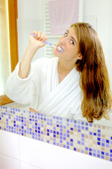 Cute woman washing teeth in bathroom in front of mirror