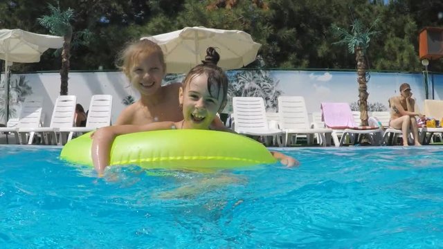 Children swim in the pool. Sisters on the inflatable circle in the pool.
