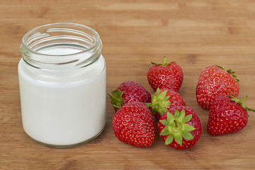 Yogurt in glass jar and strawberries on a wood background - close up
