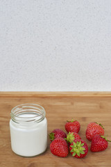 Yogurt in glass jar and strawberries on a wood background - vertical