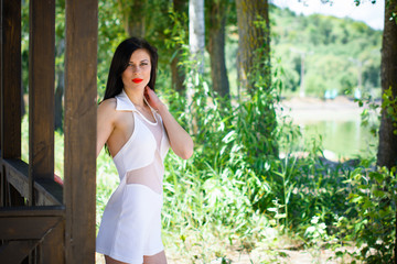 Naklejka na ściany i meble Pretty woman in white cut dress, bright make up on vacation rest and posing near trees in a beach garden