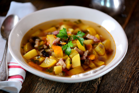Soup of yellow zucchini with potatoes, carrots, onions, mushrooms, parsley and bacon on an old wooden background.