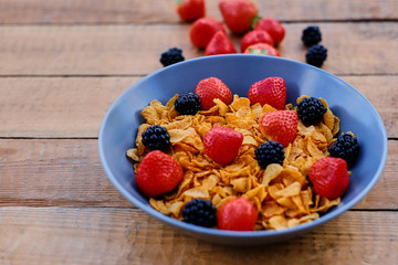 Corn flakes on a strawberry and blackberry on a plate.