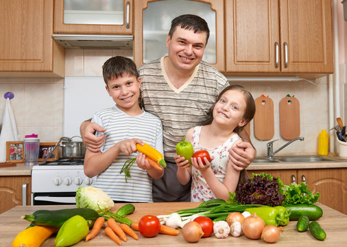 Father and two children, girl and boy, having fun with fruits and vegetables in home kitchen interior. Healthy food concept. Happy family.