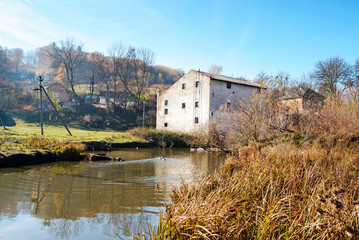 Fototapeta na wymiar Autumn landscape of the countryside: old non-working watermill near greenfields and flowing river