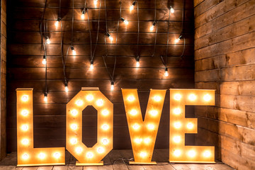 Luminous letters love.Volumetric letters on a wooden background with a garland of incandescent lamps