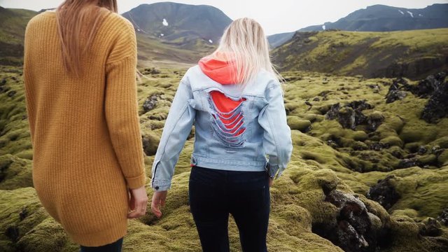Back view of two tourists woman hiking together in Iceland. Girls walking through the lava field covered moss.