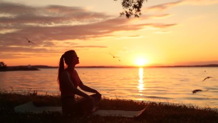Outlines of a woman meditating by the lake at sunset. A sense of calm and peace.