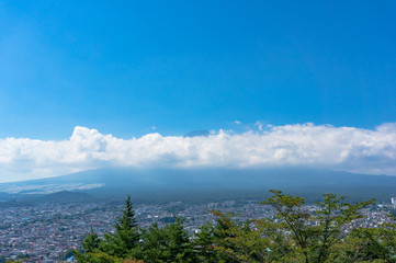 Fototapeta premium Aerial view of Fujiyoshida town and Mount Fuji peaking over clouds on sunny day