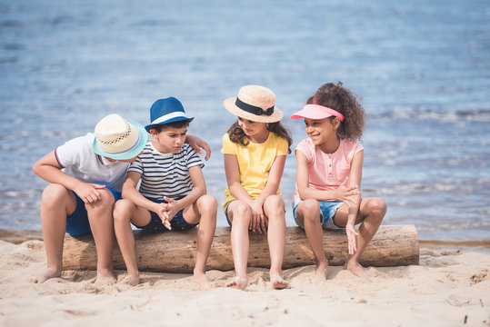 multiethnic little children sitting on wooden trunk at seaside