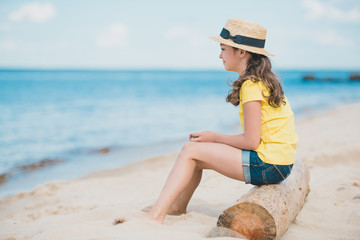 side view of cute little girl sitting on wooden trunk on sandy beach