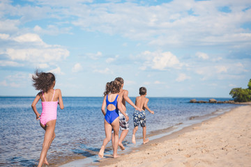 back view of children in swimsuits running on sandy beach