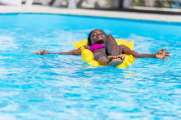 African american woman floating on inflatable mattress in swimming pool