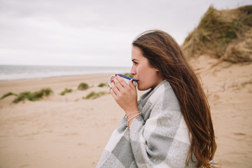 Young woman with cup of hot chocolate on the beach