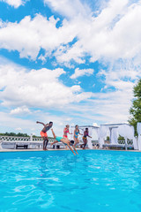 Group of beautiful young multiethnic people looking happy while jumping into the swimming pool together