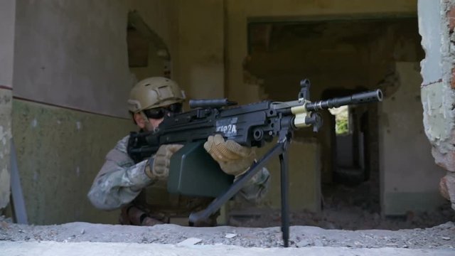 Slow motion of armed soldier in camouflage with machine gun rifle looking out the window