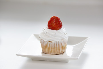 Sweet capcake with red strawberry on white plate