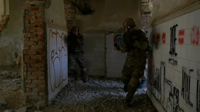 Slow motion of military soldiers running into a ruined building practicing maneuvers training