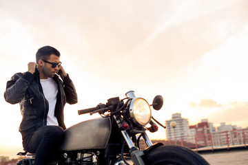 Handsome rider guy with beard and mustache smoking cigaret and correct biker jacket sit on classic...