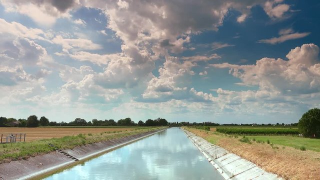 clouds over irrigation channel, water flowing to supply cultivated fields in Italian countryside in color graded clip