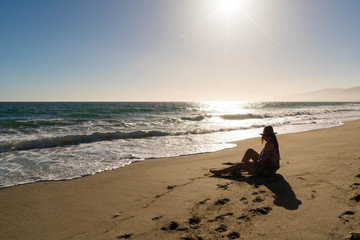 Woman Sits on Beach at Sunset