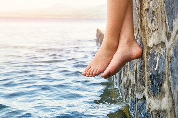  Wet bare girl's feet dangling from the jetty  - obrazy, fototapety, plakaty