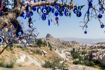 Evil Eye Beads on Tree and Fairy tale chimneys on background of blue sky in Guvercinlik Valley,Goreme,Turkey.Branches of the old tree decorated with the eye-shaped amulets