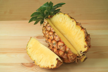 Piece of fresh ripe pineapple cut from the whole fruit on wooden table 