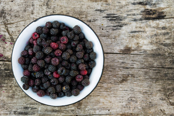 Ripe blackberries in rustic bowl on old wooden background. Top view