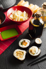Sushi rolls, wasabi, ginger, vinegar and soy sauce on black table