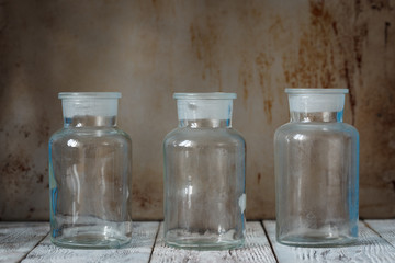 Three empty glass bottles on the white wood surface and in front of the shabby wall.
