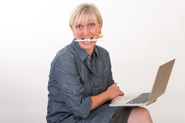 beautiful european mid aged woman working at a laptop biting on pencil - studio shot in front of light background