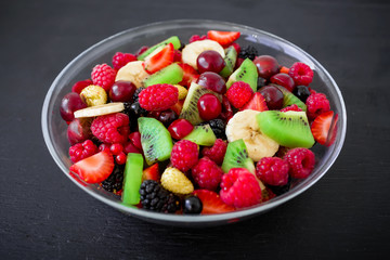Natural breakfast, fruit salad in glass plate on dark background.