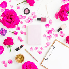 Obraz na płótnie Canvas Desk with cosmetics - lipstick, eye shadows, nail polish, pink roses and clipboard, notebook, pen on white background. Flat lay, top view.