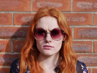 Profile of cute red haired girl with glasses against brick wall