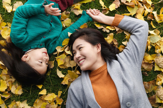 Mother and daughter lying on lawn in park in autumn