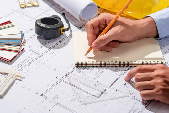 Working on blueprints. Construction project with hands writing on notebook.
